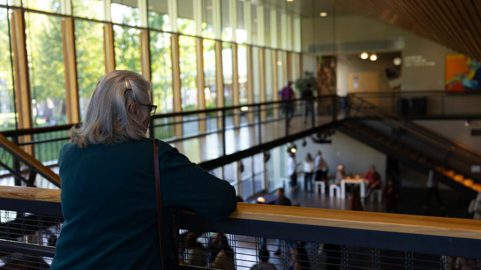 Person with short hair and glasses, overlooking the balcony to the crowd below at The Center