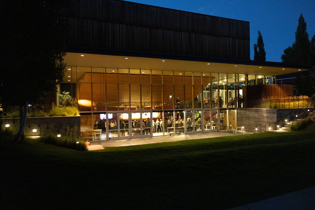 The exterior of The Center at dusk, with the lights inside lighting up the interior showing people inside