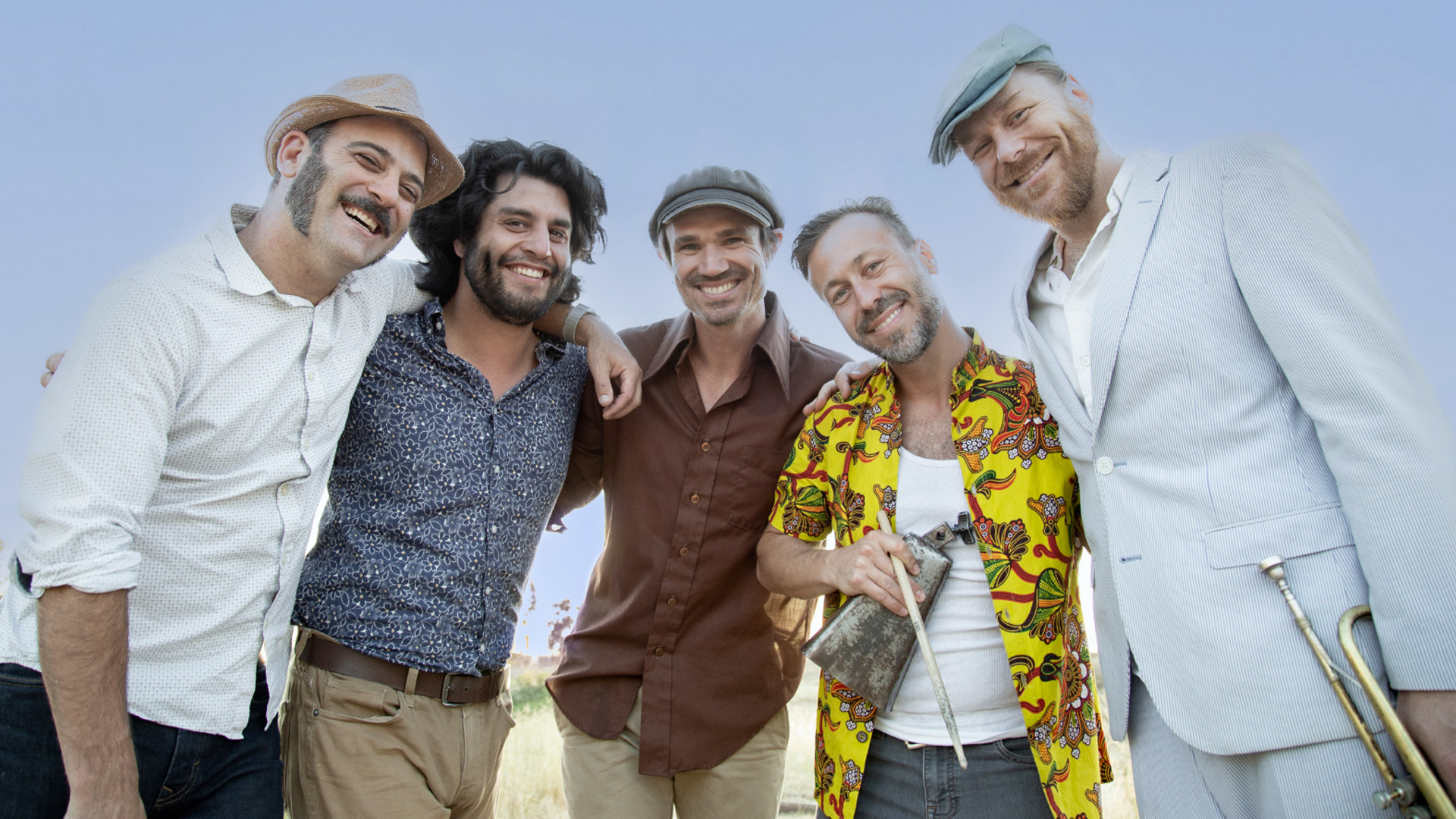 Five members of the California Honeydrops smiling at the camera, two people holding their instruments