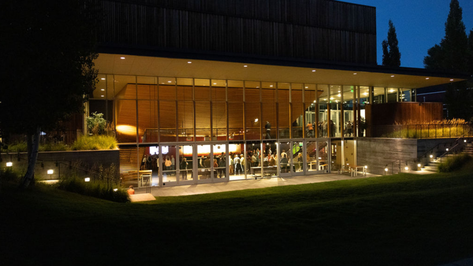 The exterior of The Center at dusk, with the lights from inside illuminating the crowd inside
