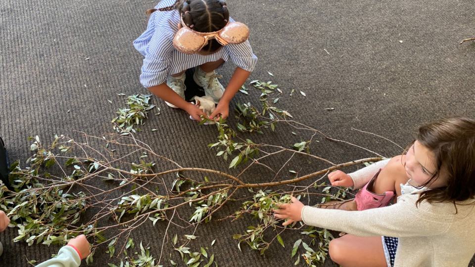 Two children partaking in a resident summer class, holding a branch of a tree on the floor