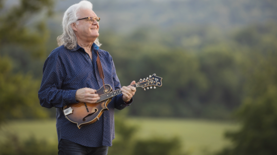 An older gentleman with long white hair playing an instrument outside
