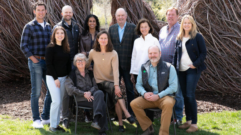 A group shot of the team, three are sat in chairs, two women have their legs crossed and everyone is smiling and smartly dressed