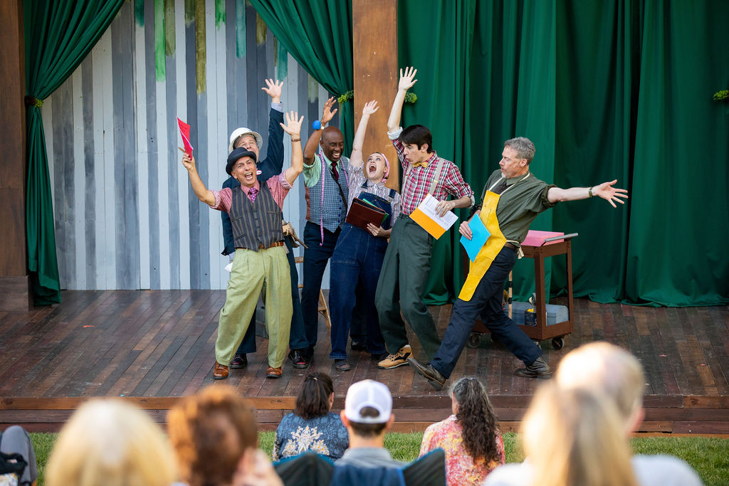 A group of actors on stage performing with arms raised at The Center Amphitheater outdoor venue in Jackson Hole, Wyoming