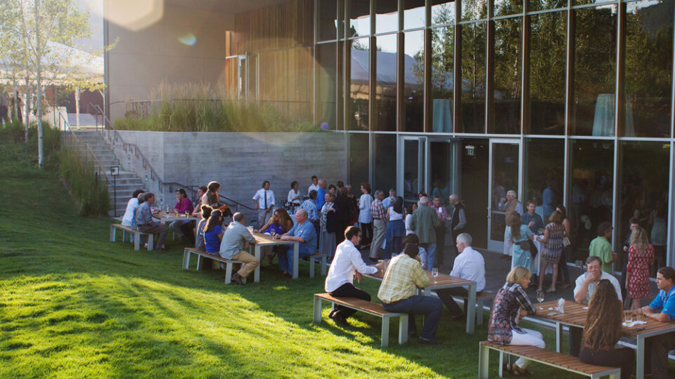 The outside of the JH center with people sat on large tables and benches on the grass